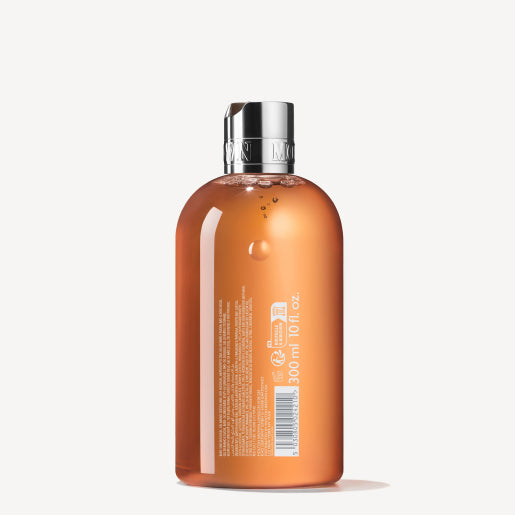 The Sunlit Clementine & Vetiver Bath & Shower Gel 300ml comes in a clear orange bottle with a silver cap, white text, and a barcode, all displayed on a plain white background.