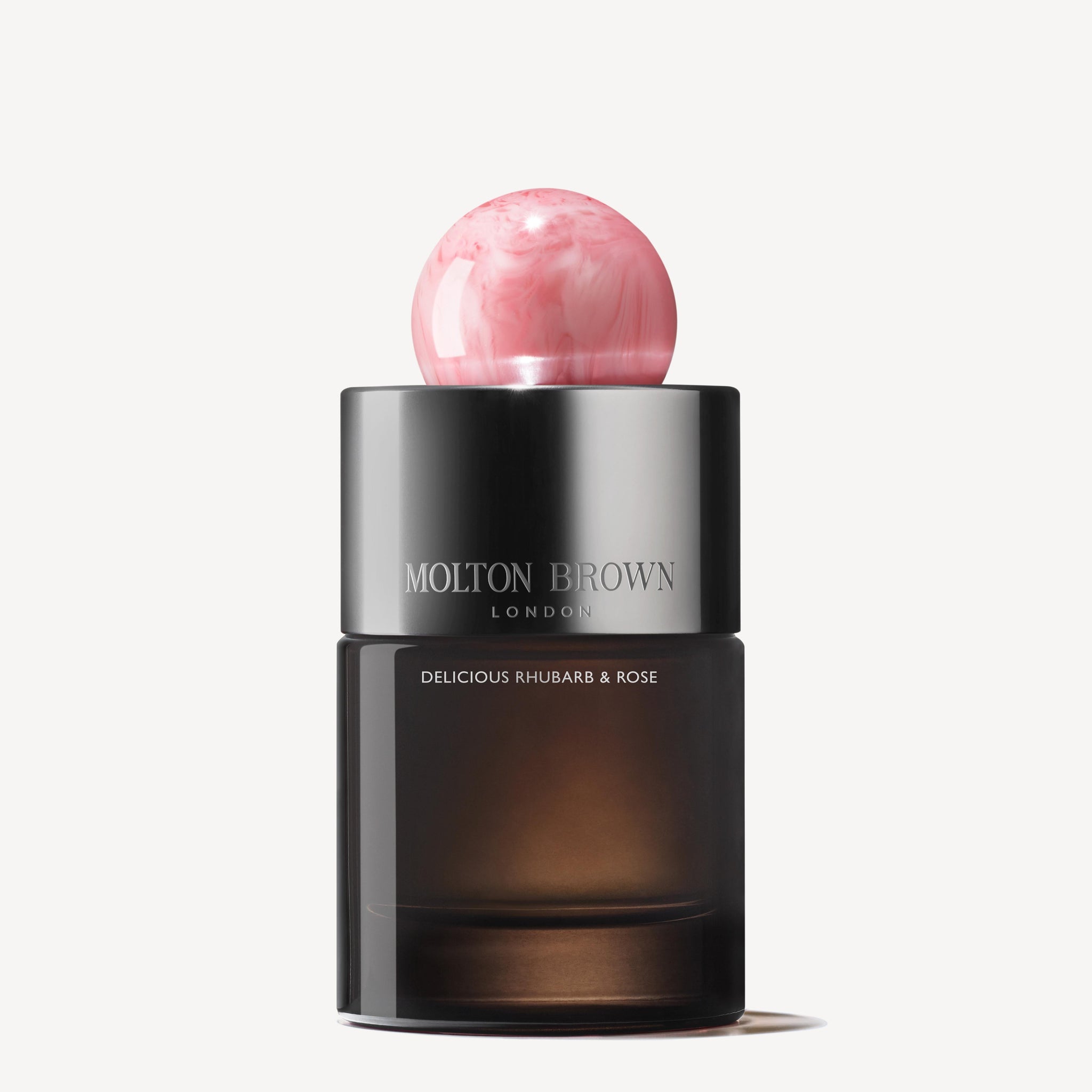 The Delicious Rhubarb & Rose Eau de Parfum 100ml features a dark glass bottle with silver accents and a round, pink marbled cap, exuding peony notes against a white background.