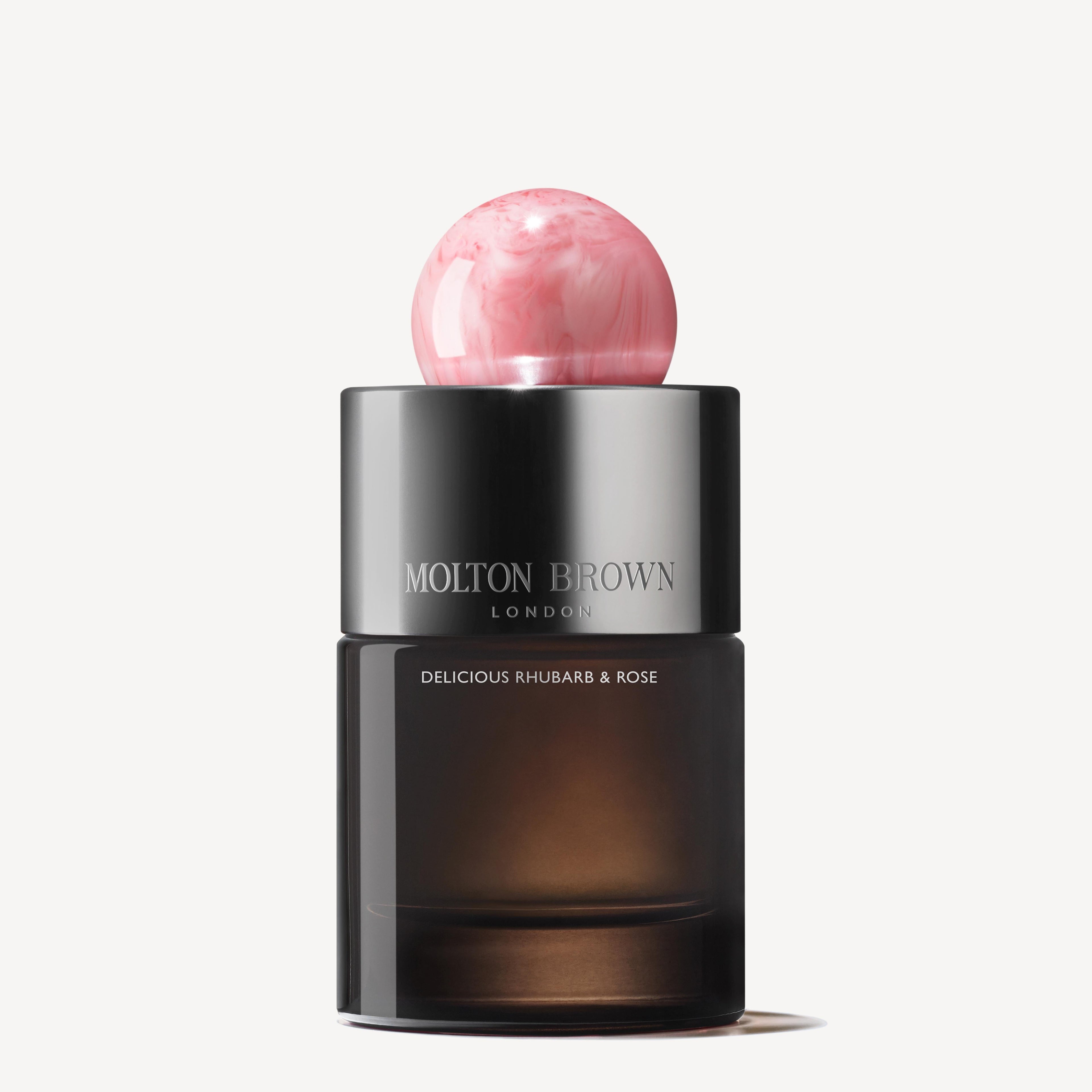 The Delicious Rhubarb & Rose Eau de Parfum 100ml features a dark glass bottle with silver accents and a round, pink marbled cap, exuding peony notes against a white background.