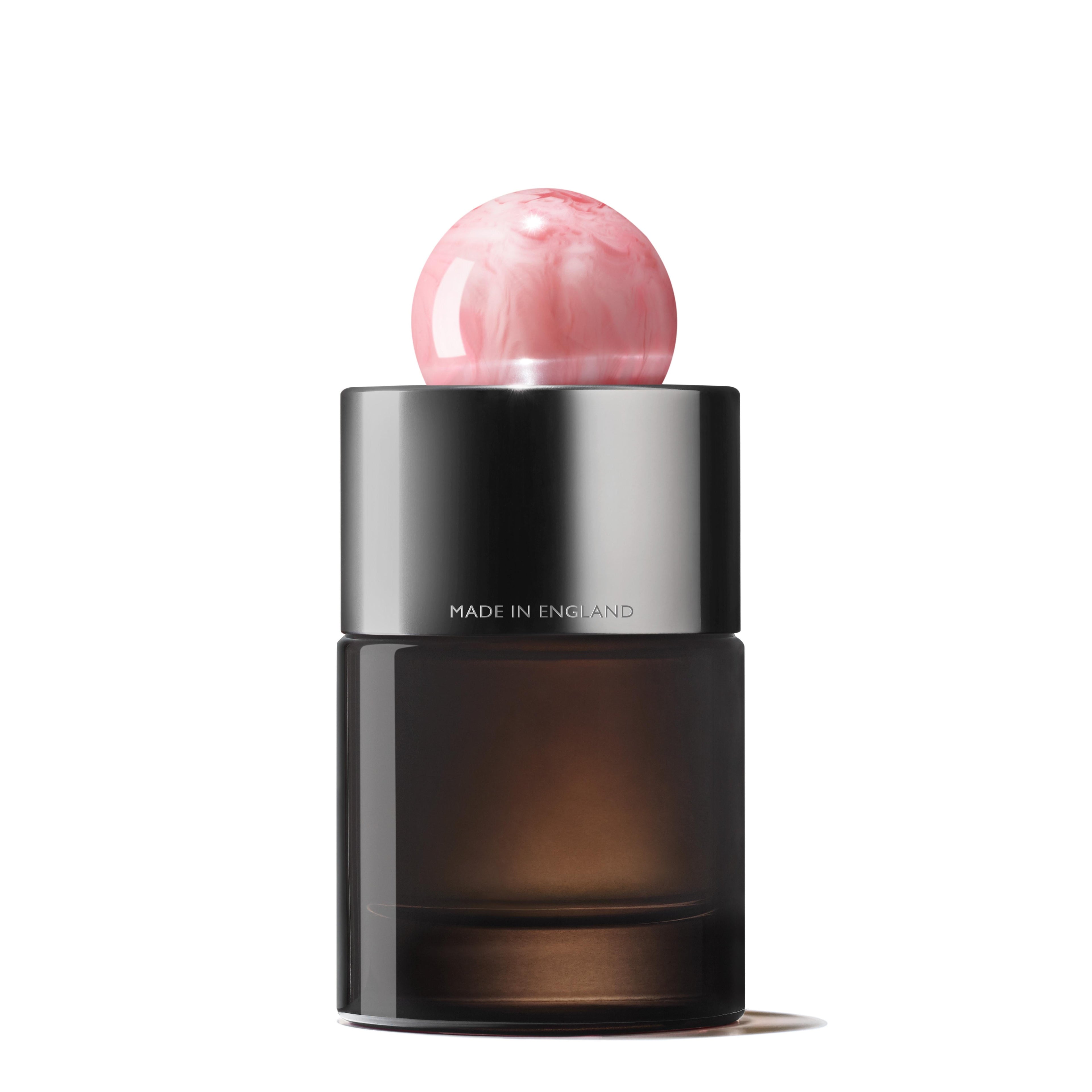 A dark glass bottle of Delicious Rhubarb & Rose Eau de Parfum 100ml with a metallic silver band and pink marble-like round cap. "MADE IN ENGLAND" is etched on the silver. Shot on a plain white background—perfect for peony fragrance lovers.