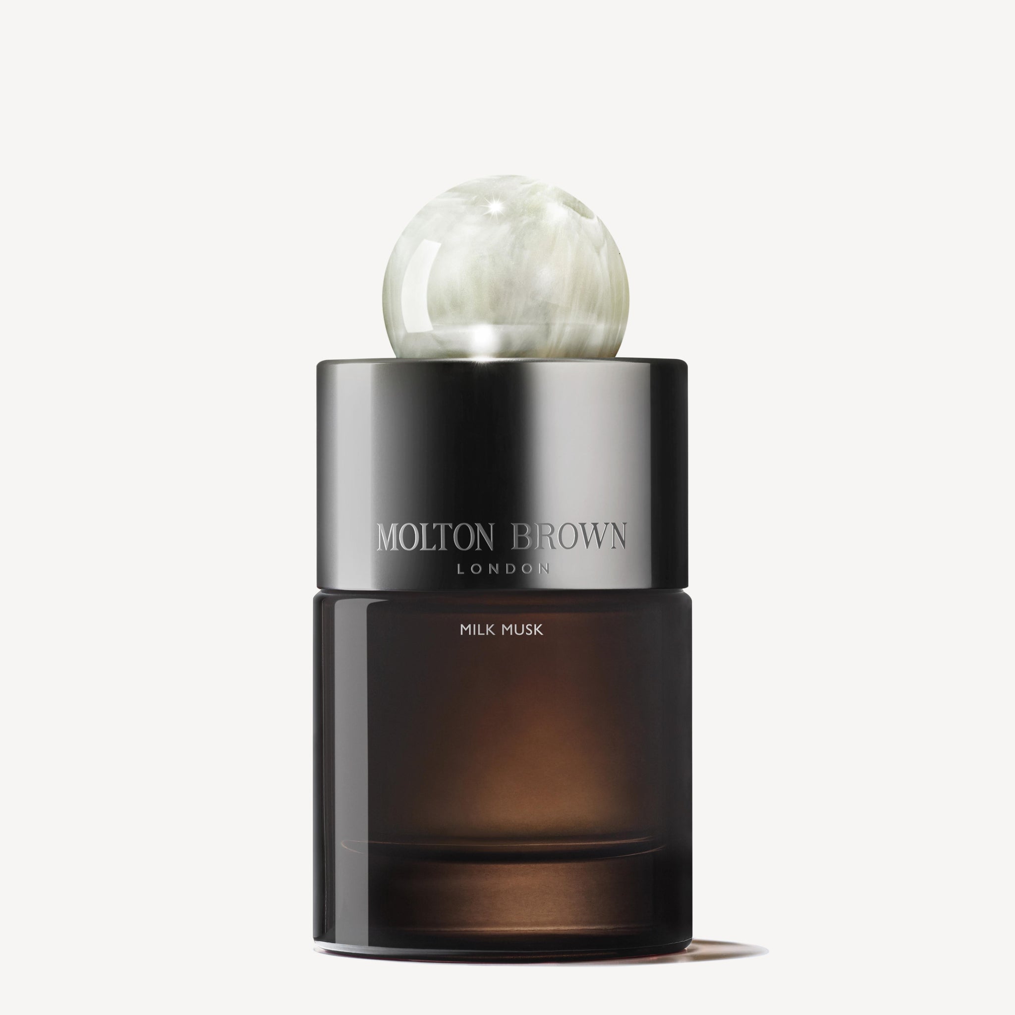 A 100ml Milk Musk Eau de Parfum bottle with a dark translucent base, shiny silver label, and round marble-like cap is showcased against a plain white background, highlighting its soothing musk-inspired elegance.