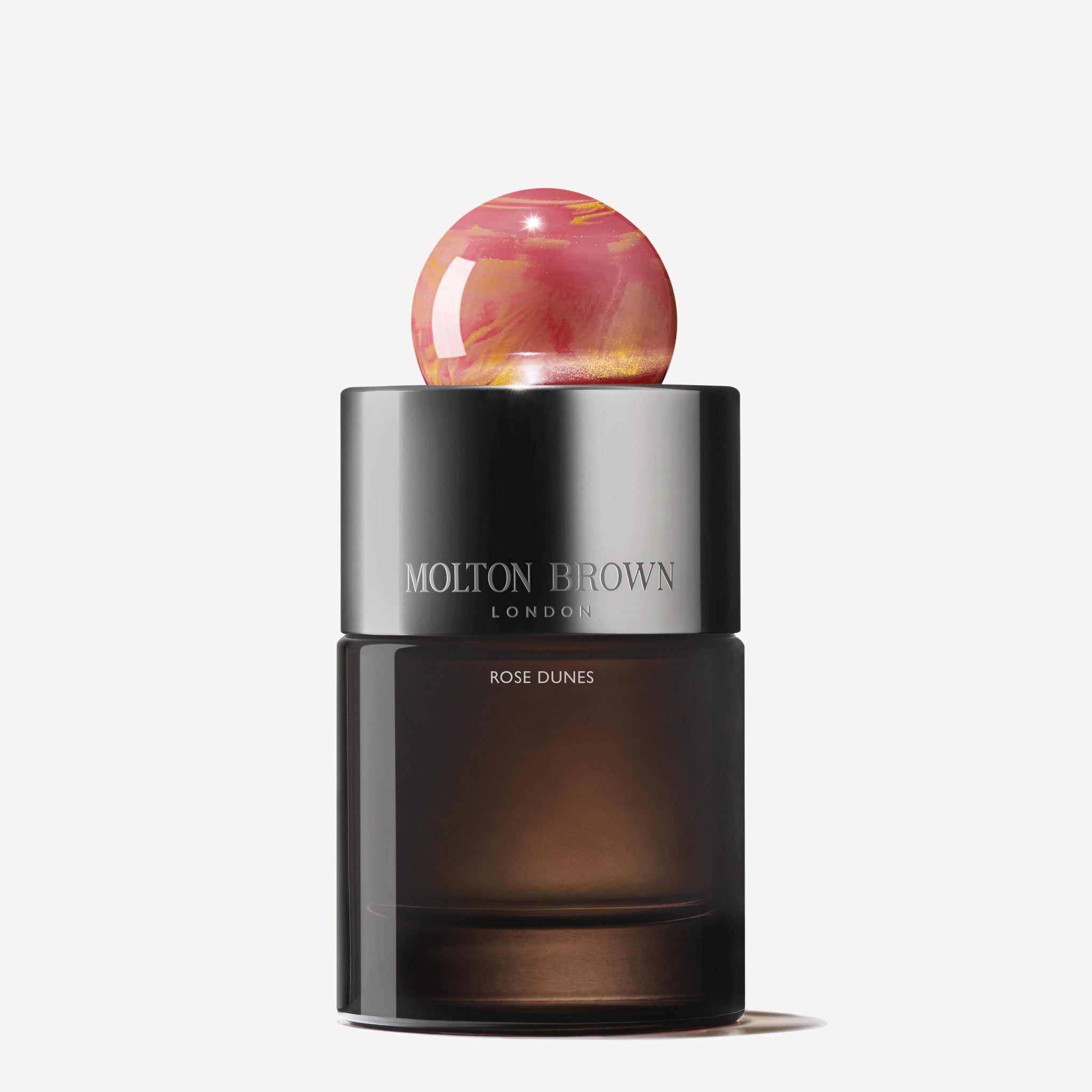 A dark glass bottle of Rose Dunes Eau de Parfum 100ml, with a metallic cap and a round pink marbled stopper, evokes Arabian desert mystique against a plain white background.