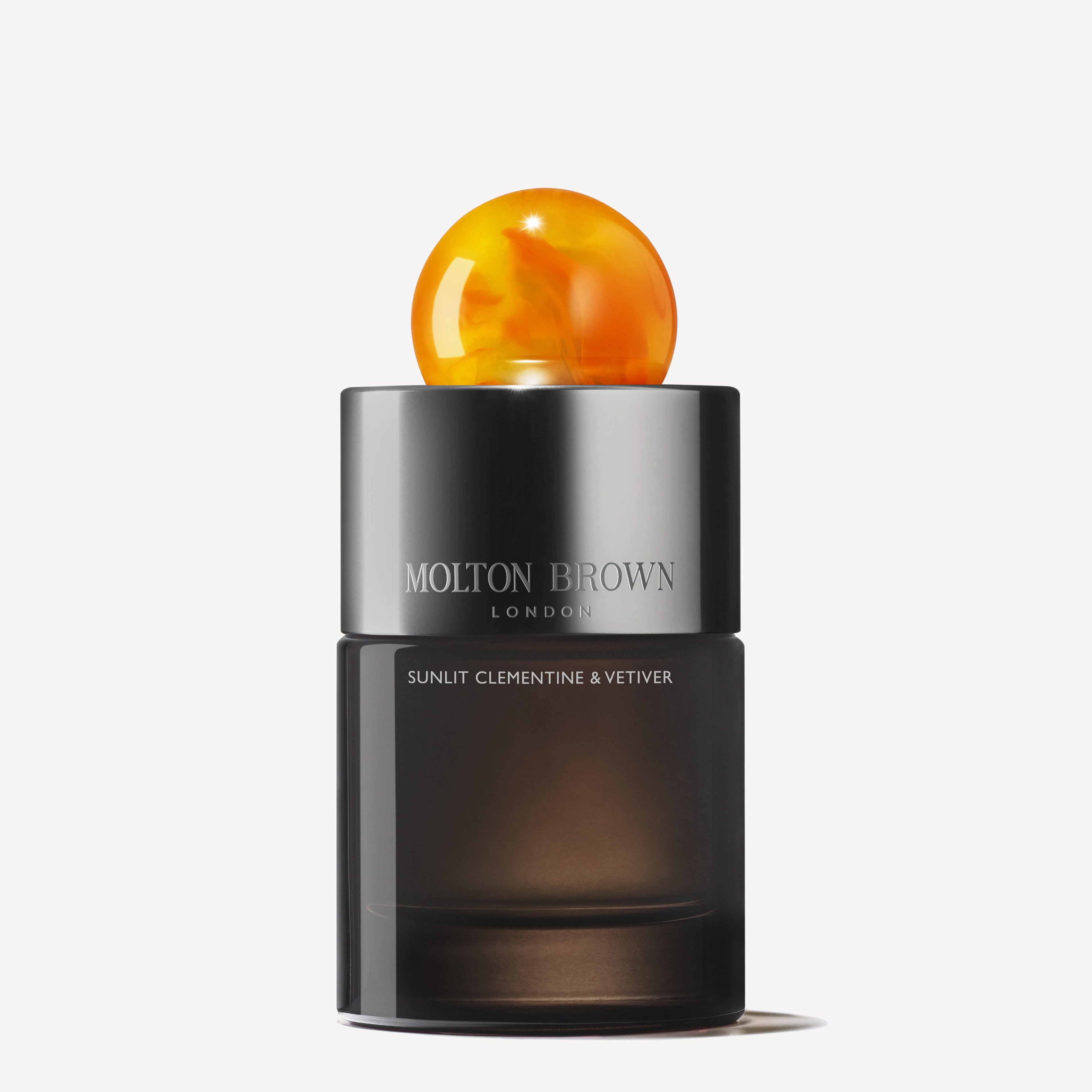 A 100ml Sunlit Clementine & Vetiver Eau de Parfum bottle by Molton Brown, with a sleek dark base and round marbled orange cap, shown on a white background.