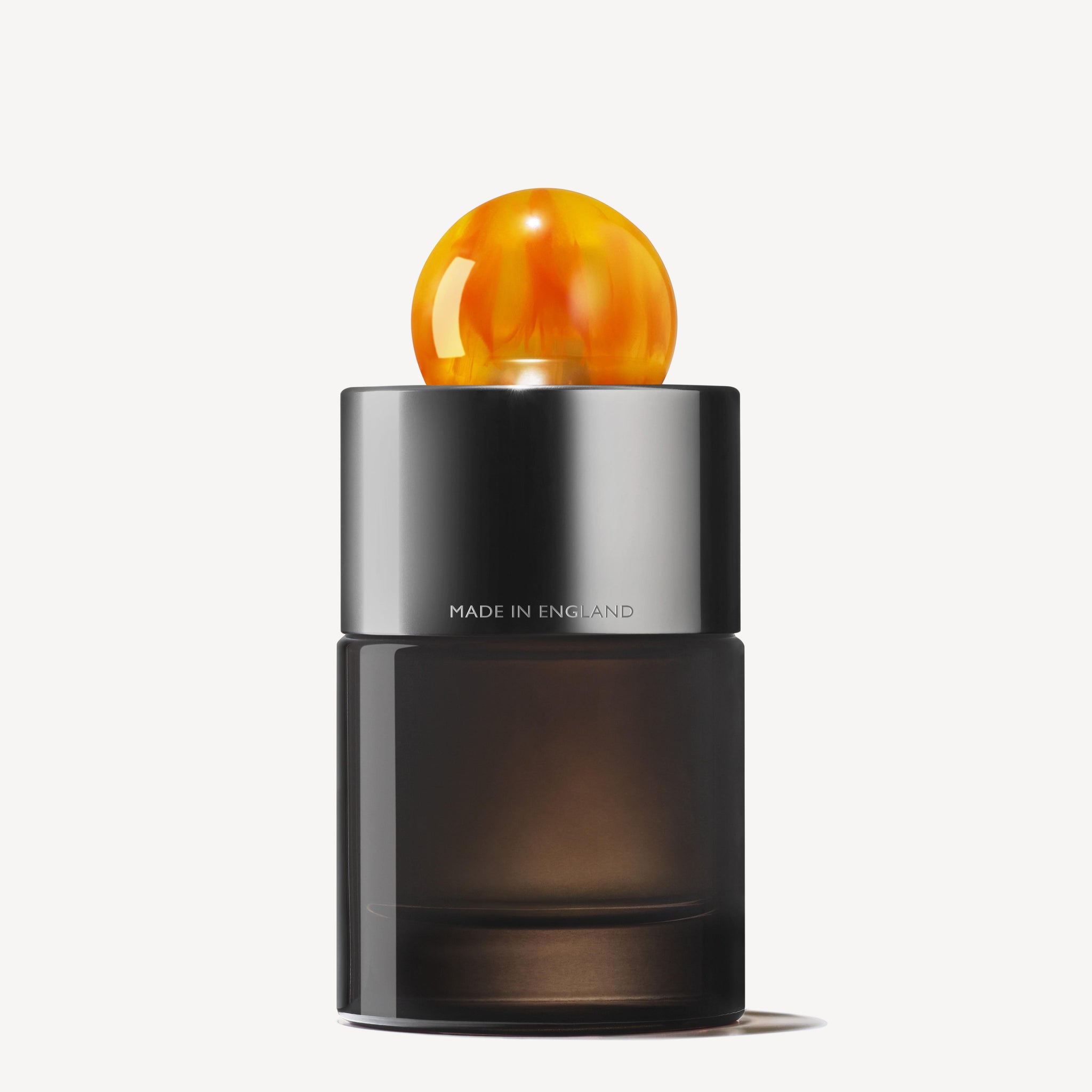 The Sunlit Clementine & Vetiver Eau de Parfum 100ml features a sleek, dark glass bottle with a shiny silver collar printed with "MADE IN ENGLAND" and a round amber cap, embodying elegance against a plain white background.